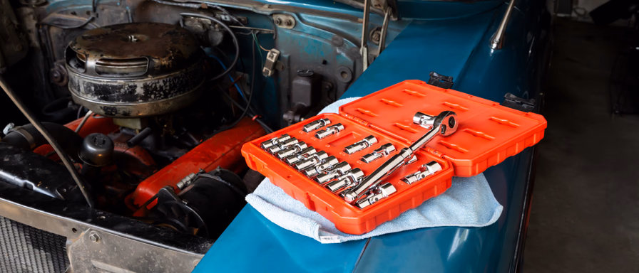 A vintage blue car with its engine hood open and a set of wrenches next to the engine.